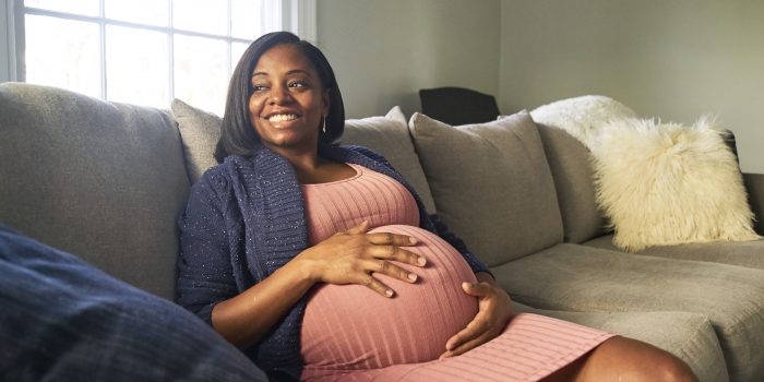 Expectant black mom sits on couch holding her belly