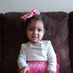 Baby save Nevaeh sits on a couch wearing a pink skirt and pink bow