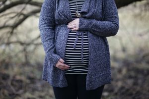 A pregnant white woman wearing a striped shirt and sweatercradles her belly