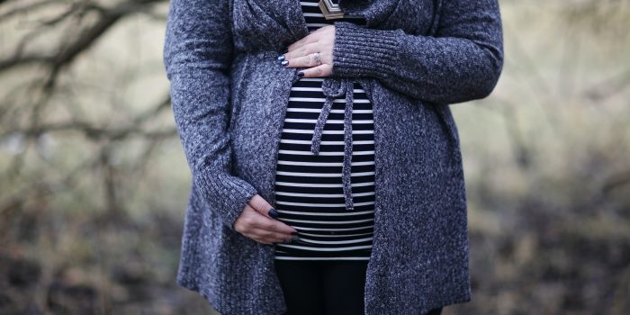 A pregnant white woman wearing a striped shirt and sweatercradles her belly