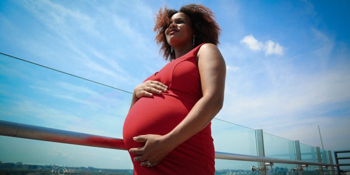 A pregnant Black woman holds her belly with a blue sky in the background