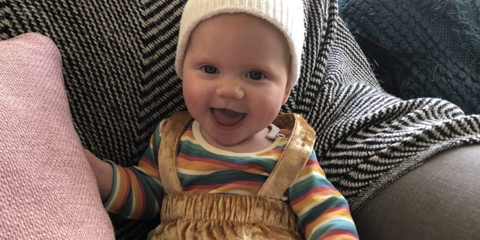 Smiling, happy baby wearing a hat sits on a couch