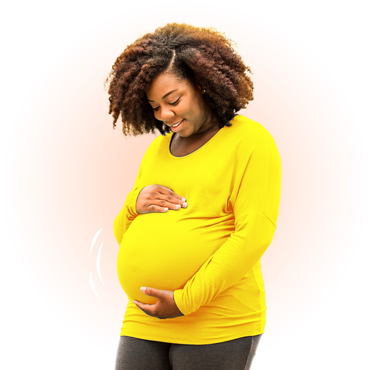 A pregnant woman wearing a yellow long sleeve shirt smiles as she cradles her stomach.