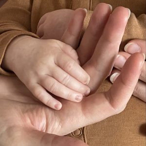 A newborn's hand rests in her mom's hand.