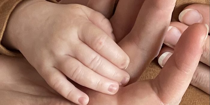 A newborn's hand rests in her mom's hand.