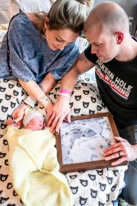 Missouri Ambassador Erica Bailey with her newborn son, Bear, and her husband. The couple is looking at a photo of their son Rhoan, who was born still in March 2020.