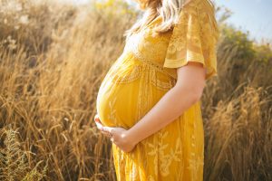 Pregnant woman in yellow dress standing in field resting her hands on her belly