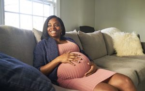 Expectant black mom sits on couch holding her belly