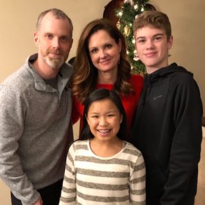 Amy Romanin stands, center, in front of Christmas tree with her son, daughter and husband