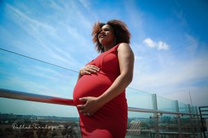 A pregnant Black woman holds her belly with a blue sky in the background