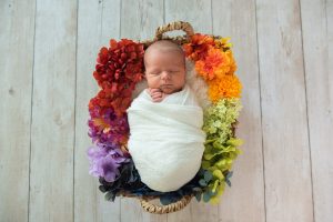 A baby swaddled in a white blanket sleeps in a nest of colorful flowers