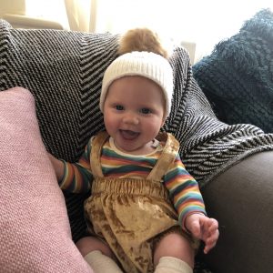 Smiling, happy baby wearing a hat sits on a couch