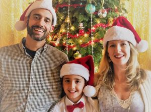 A family wearing Santa hats stand together in front of a Christmas tree