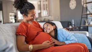 Daughter hugs belly of her pregnant mama.