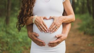 Expectant parents form a heart on mom's pregnant baby bump.