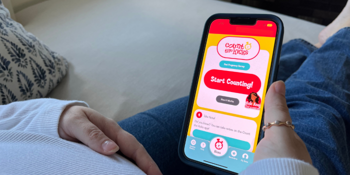 A pregnant woman holds her phone with the Count the Kicks app open on it.