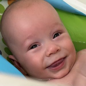 A smiling baby in a bathtub, surrounded by colorful aquatic-themed cushions.