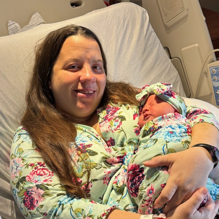 A woman in a hospital bed smiles while cradling her newborn. Both wear matching floral outfits
