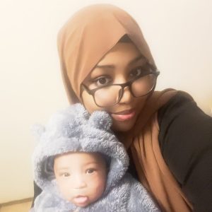 A woman with glasses and a hijab lovingly holds a baby