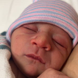 Newborn baby wearing a striped hospital hat, wrapped in a blanket, sleeping with eyes closed