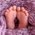 Close-up of a newborn baby's feet resting on a soft purple knitted blanket.