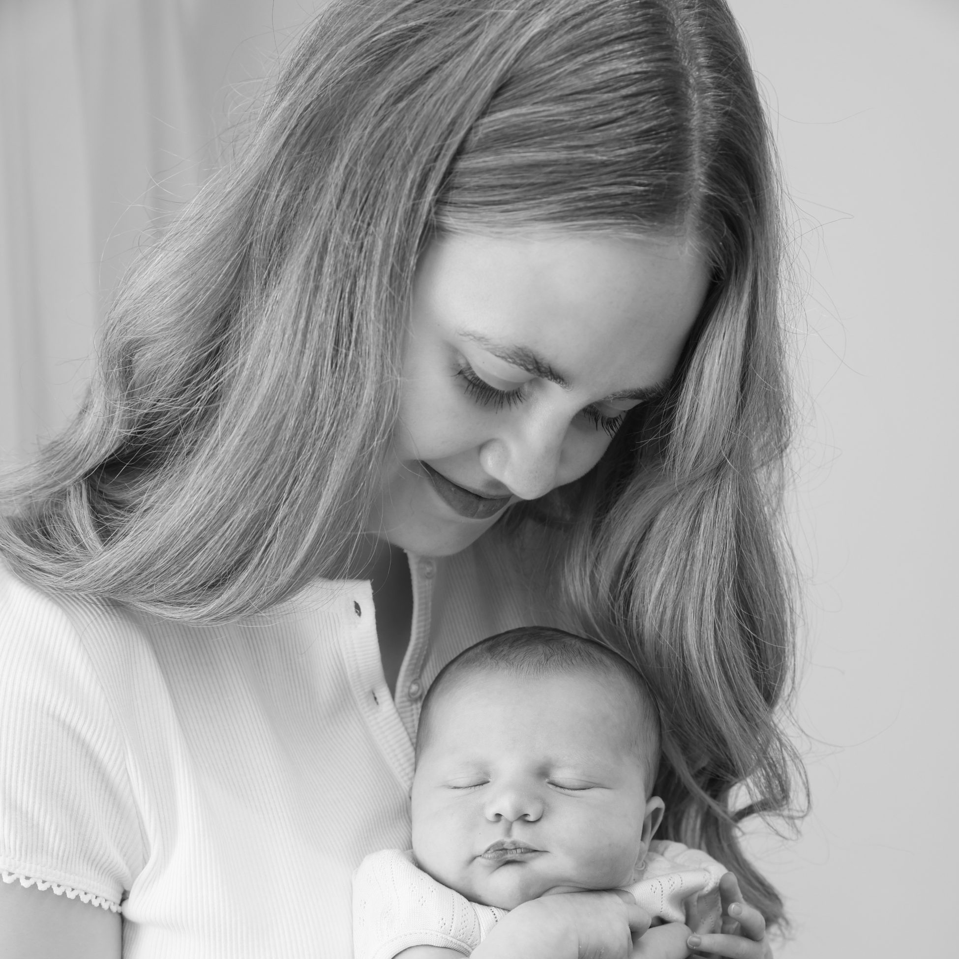 Black-and-white photo of a woman gently holding a sleeping newborn baby in her arms.
