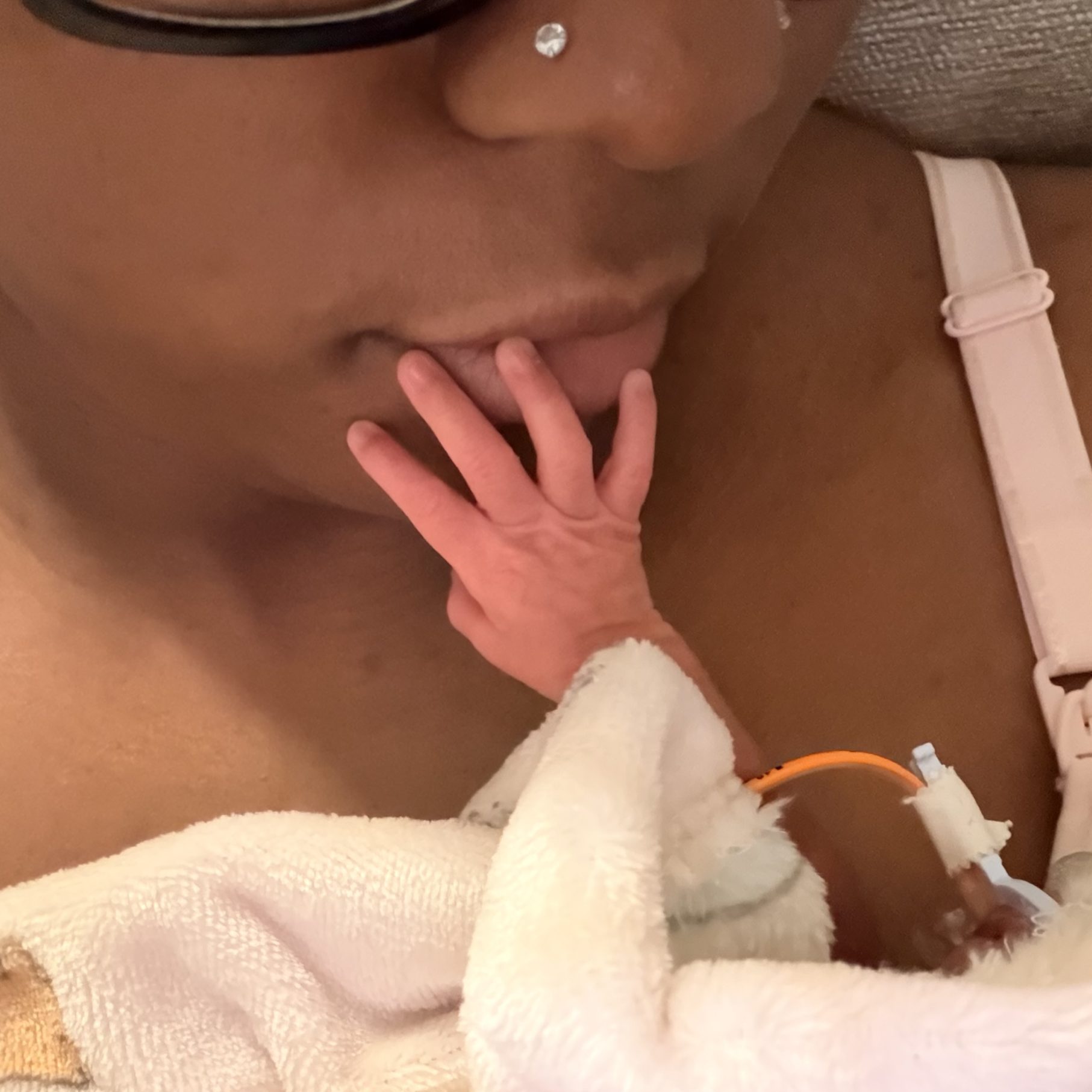 Baby’s tiny hand rests against their mother’s chest as she gently holds them wrapped in soft blankets